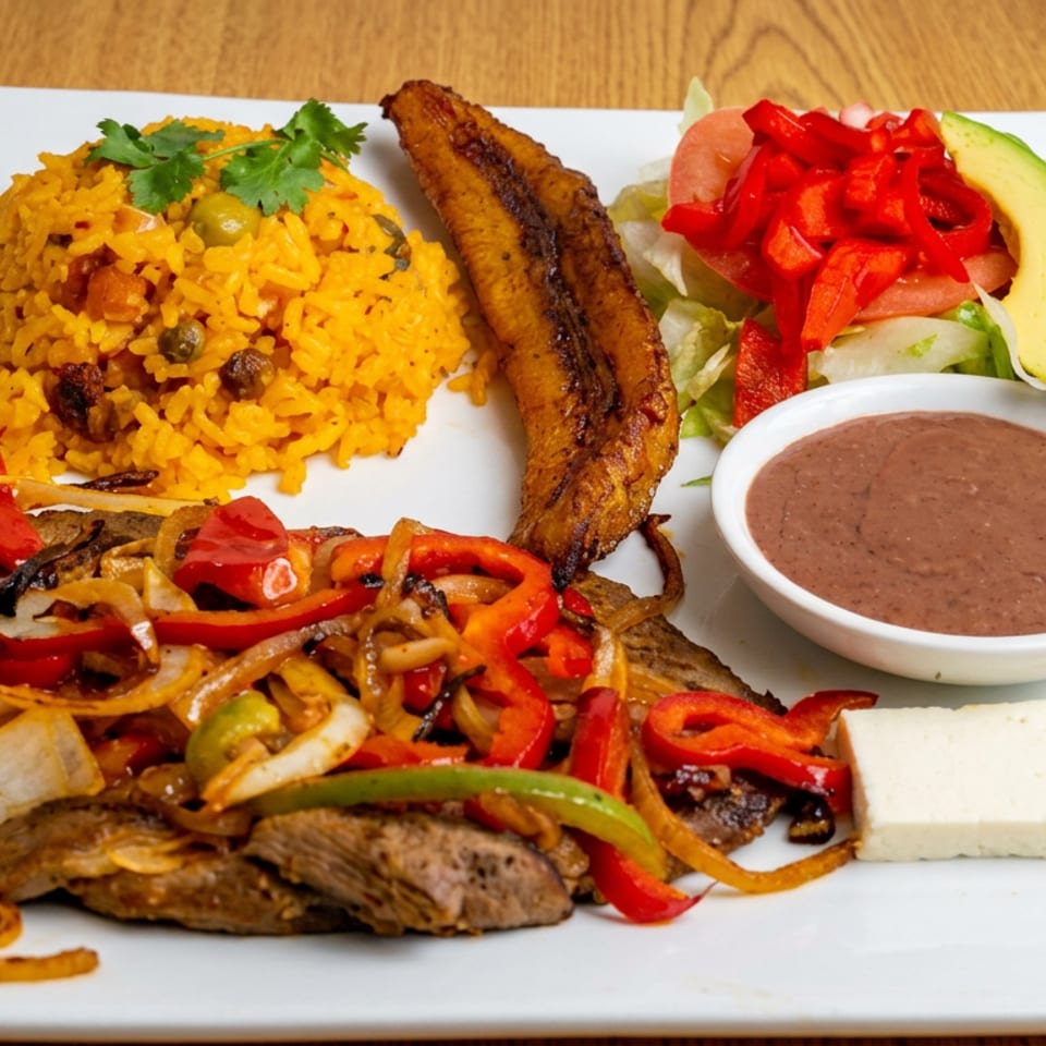 Latin American platter with grilled steak, fried plantain, yellow rice, sautéed peppers and onions, salad, beans, and avocado.
